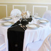 Elegant black satin table runner set for a wedding or event with white plates and glassware.