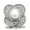 A silver snap button with a round, clear gemstone center surrounded by pave-set diamonds.