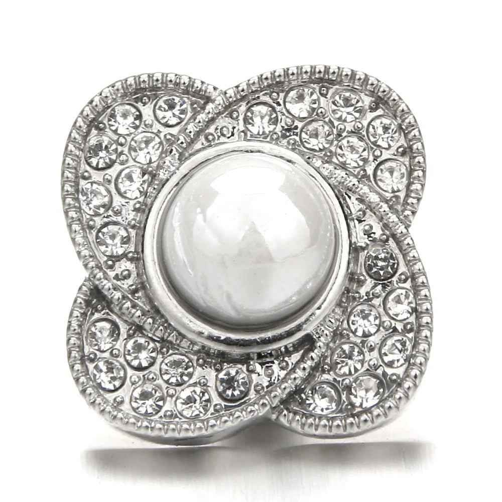 A silver snap button with a round, clear gemstone center surrounded by pave-set diamonds.