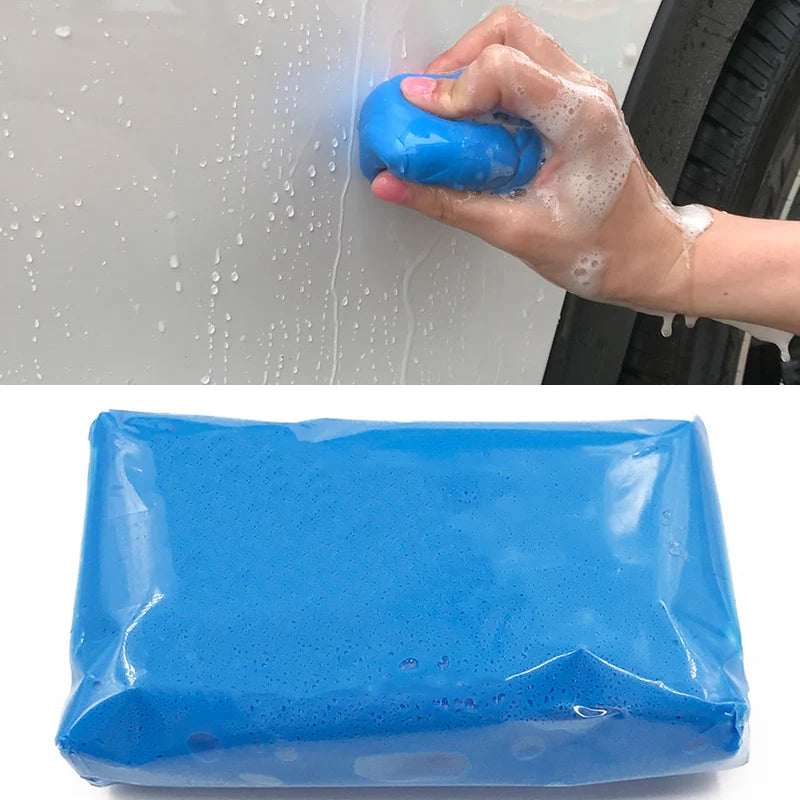 A hand applies a blue clay bar to a car surface, with a blue plastic bar visible in the foreground.