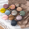 A collection of food-grade silicone pacifier cases in various pastel and neutral colors resting on a beige fabric.