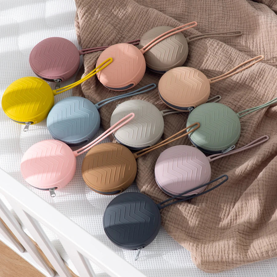A collection of food-grade silicone pacifier cases in various pastel and neutral colors resting on a beige fabric.