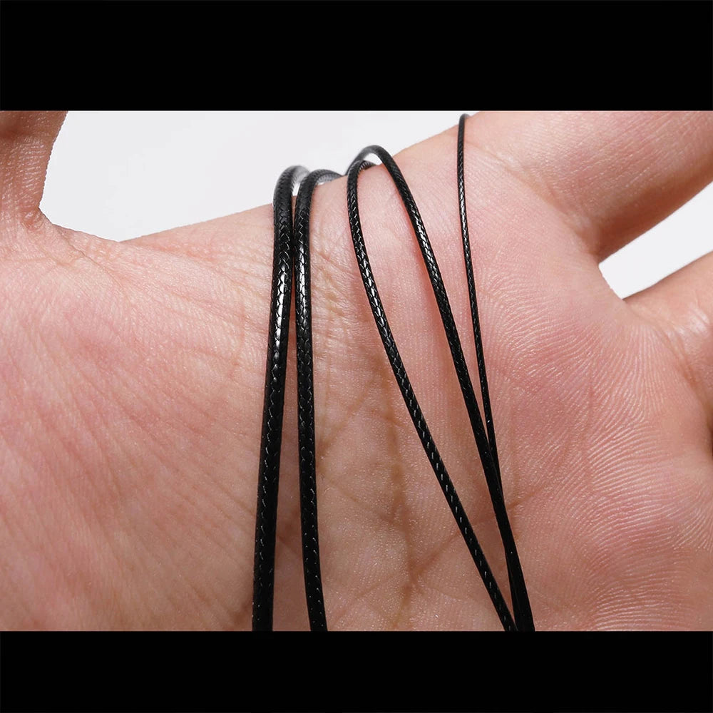 A hand holds several black waxed cotton cords used for jewelry making.