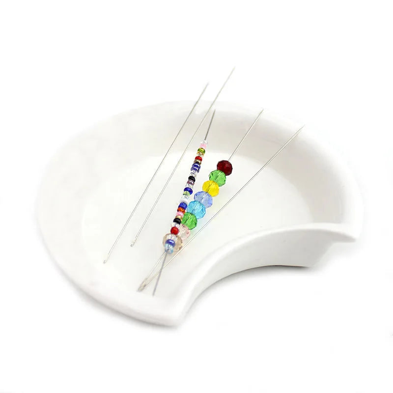 A set of stainless steel beading needles with colorful beads displayed on a white dish.