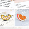 An orange slice enamel fruit brooch pin resting on a white background with blurred text.