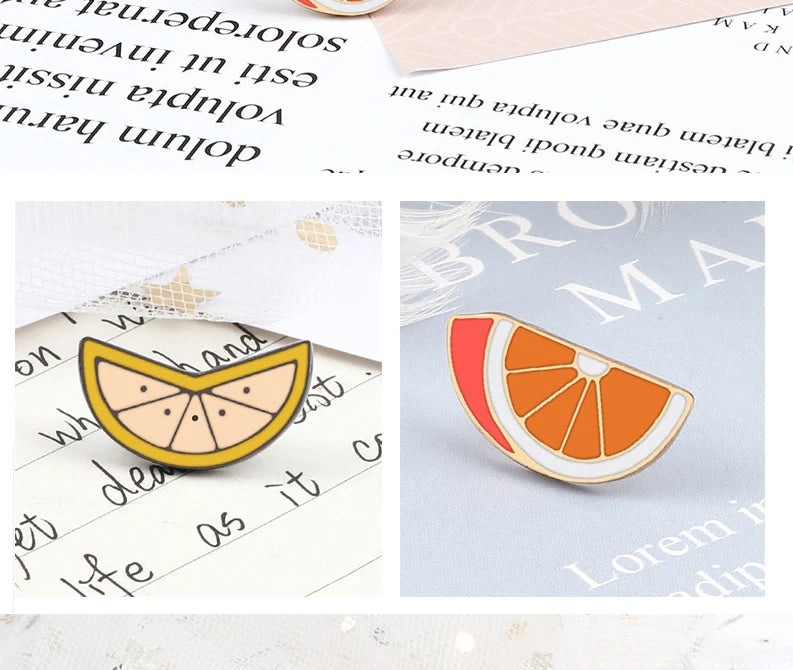 An orange slice enamel fruit brooch pin resting on a white background with blurred text.