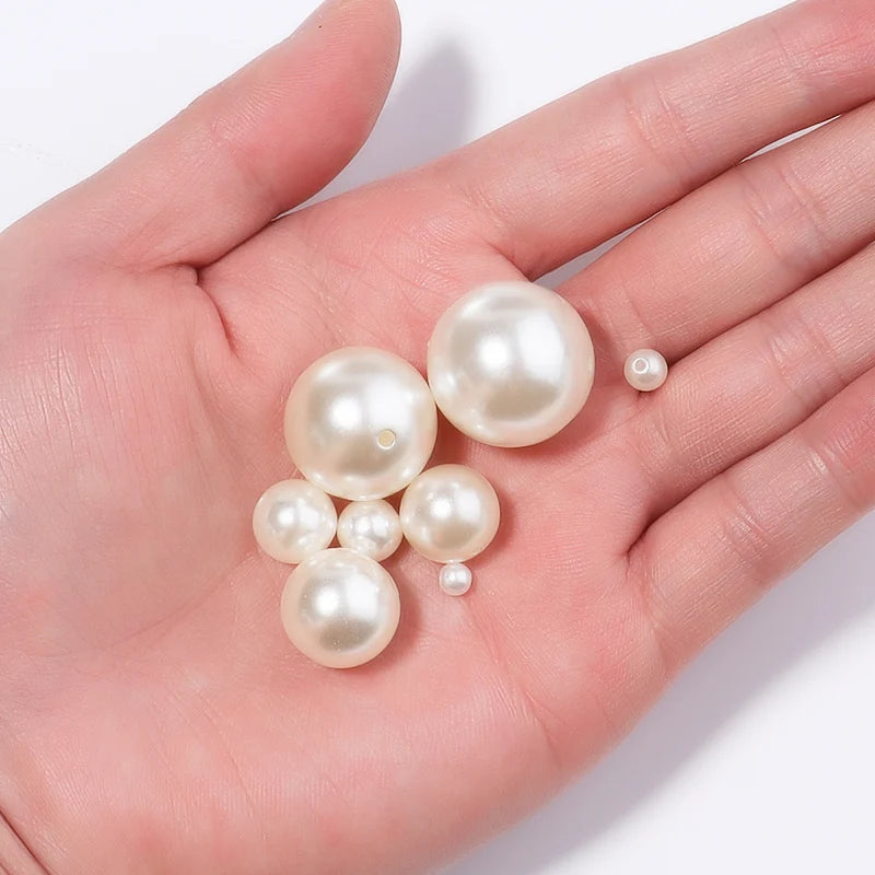 A hand holds several round, off-white imitation pearl beads for jewelry making.
