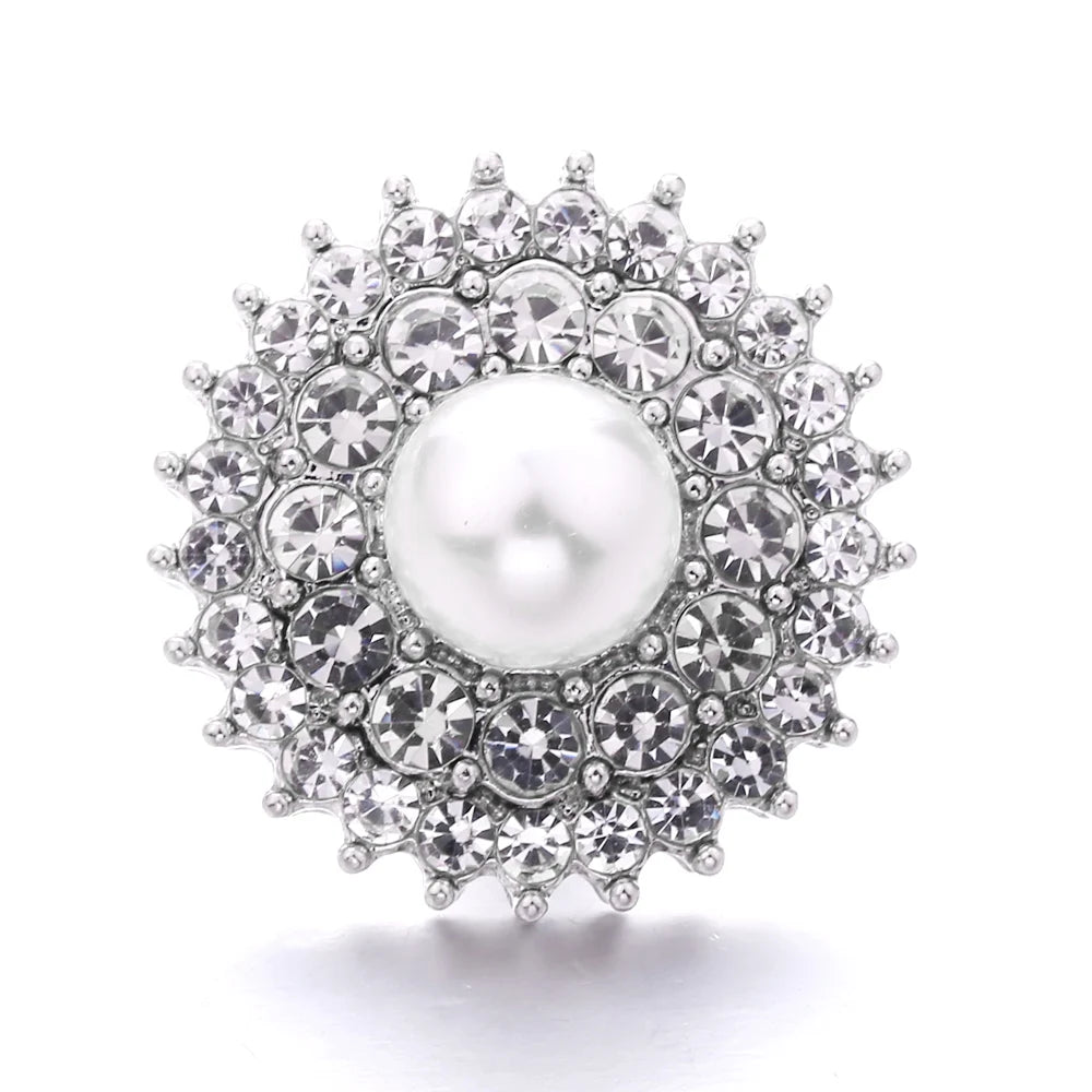 A close-up of a round, brilliant diamond-encrusted metal snap button with a central pearl.
