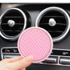 A hand holds a pink crystal rhinestone non-slip cup mat for cars, positioned in front of car air vents.