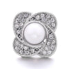 A silver-toned snap button featuring a central white pearl surrounded by pave-set clear stones.