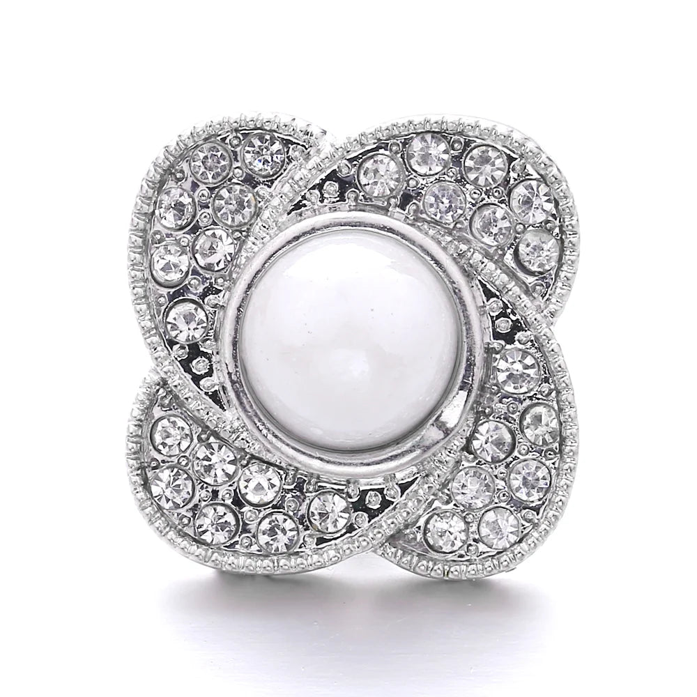 A silver-toned snap button featuring a central white pearl surrounded by pave-set clear stones.