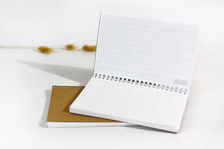 An open white spiral-bound monthly planner with a grid page and a brown cover lies on a white surface.