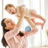 A woman is holding a baby in the air while using a food-grade silicone pacifier case.