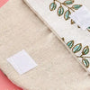 A beige cosmetic storage pouch with a natural fiber texture and embroidered green leaves.