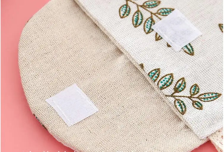 A beige cosmetic storage pouch with a natural fiber texture and embroidered green leaves.