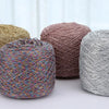 Three skeins of metallic silk crochet yarn in shades of beige, pink, and silver resting on a white surface.
