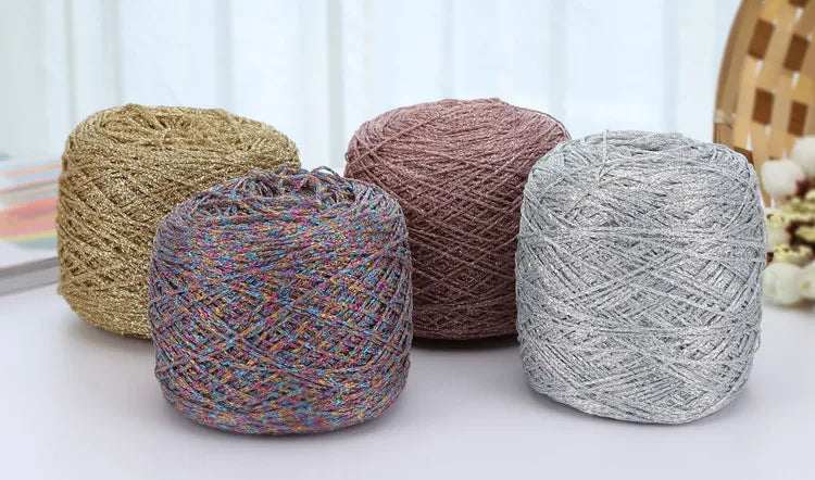Three skeins of metallic silk crochet yarn in shades of beige, pink, and silver resting on a white surface.