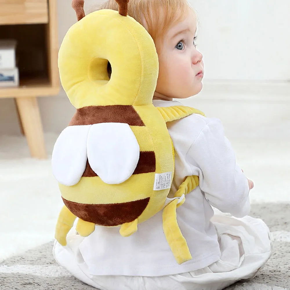A yellow stuffed bee head protector backpack worn by a toddler, sitting on a gray rug.