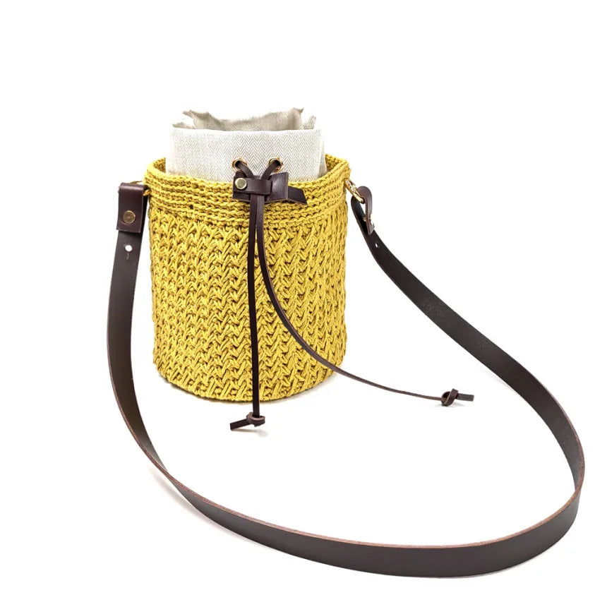 A yellow woven straw bag with a light fabric lining and a brown leather adjustable strap.