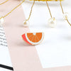 A gold-toned fruit brooch pin shaped like a sliced orange with red and white enamel details.