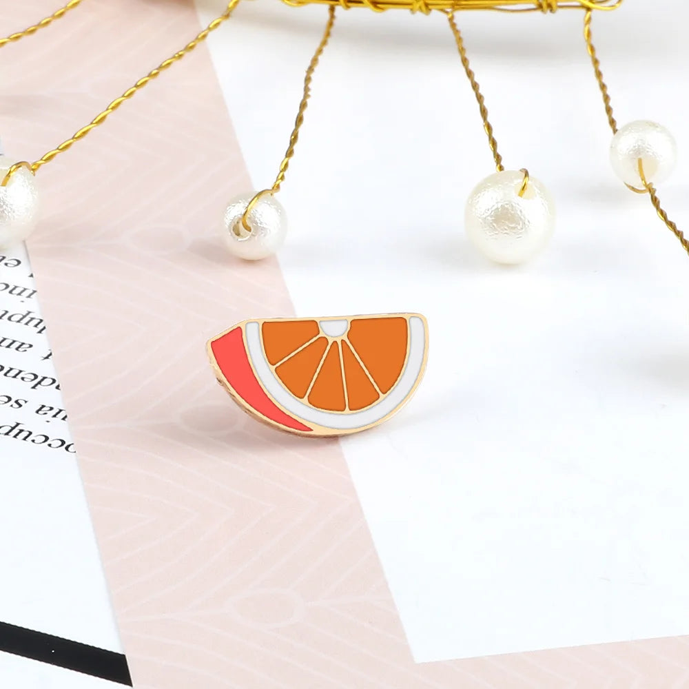 A gold-toned fruit brooch pin shaped like a sliced orange with red and white enamel details.