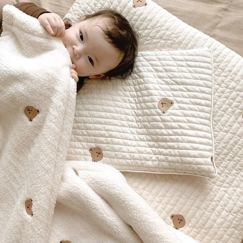 A baby is lying on a white coral fleece blanket with bear embroidery.