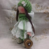 A handmade doll with long dark hair wearing a green knitted hat and white clothing.