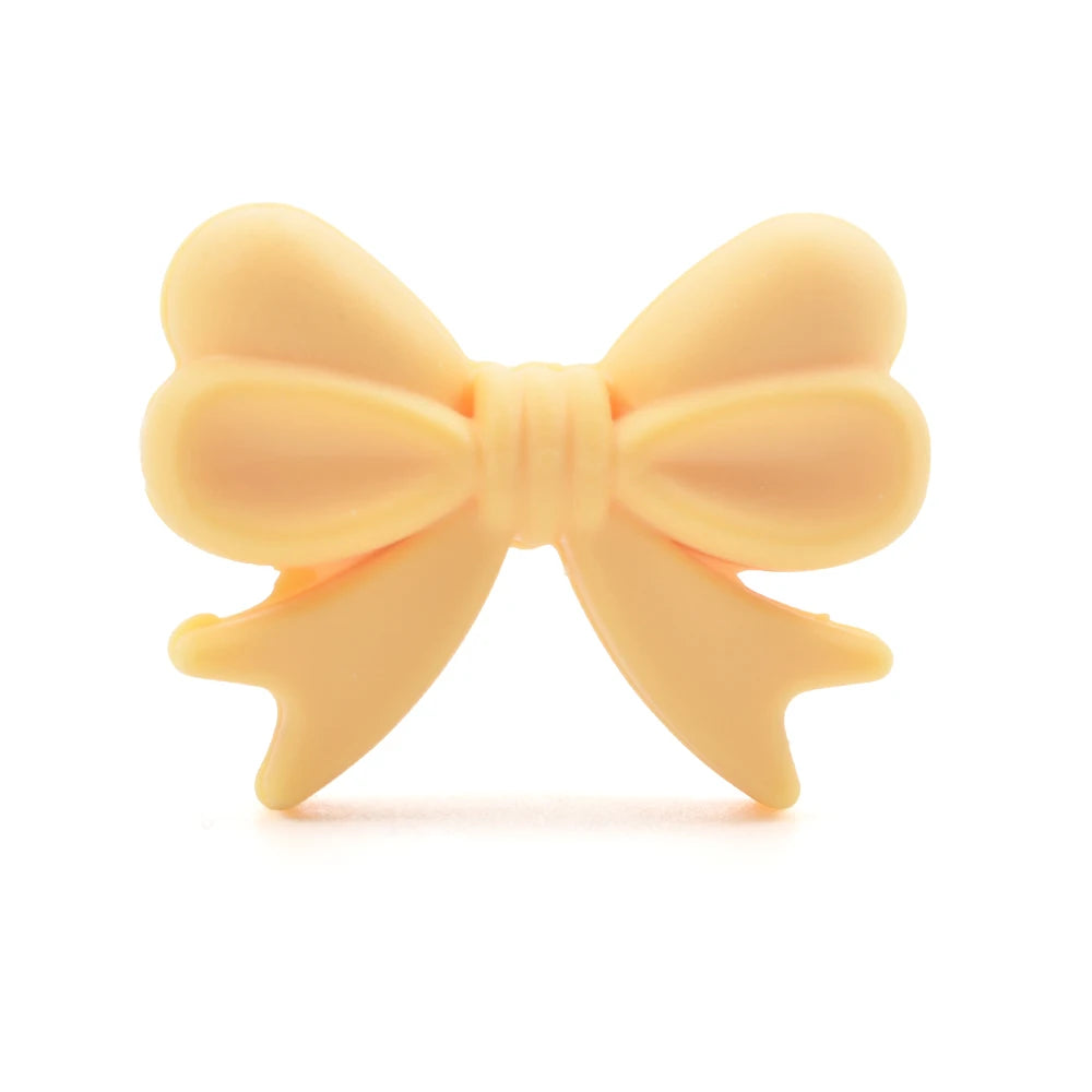 A light peach silicone bow or crown bead used for jewelry making and DIY crafts.
