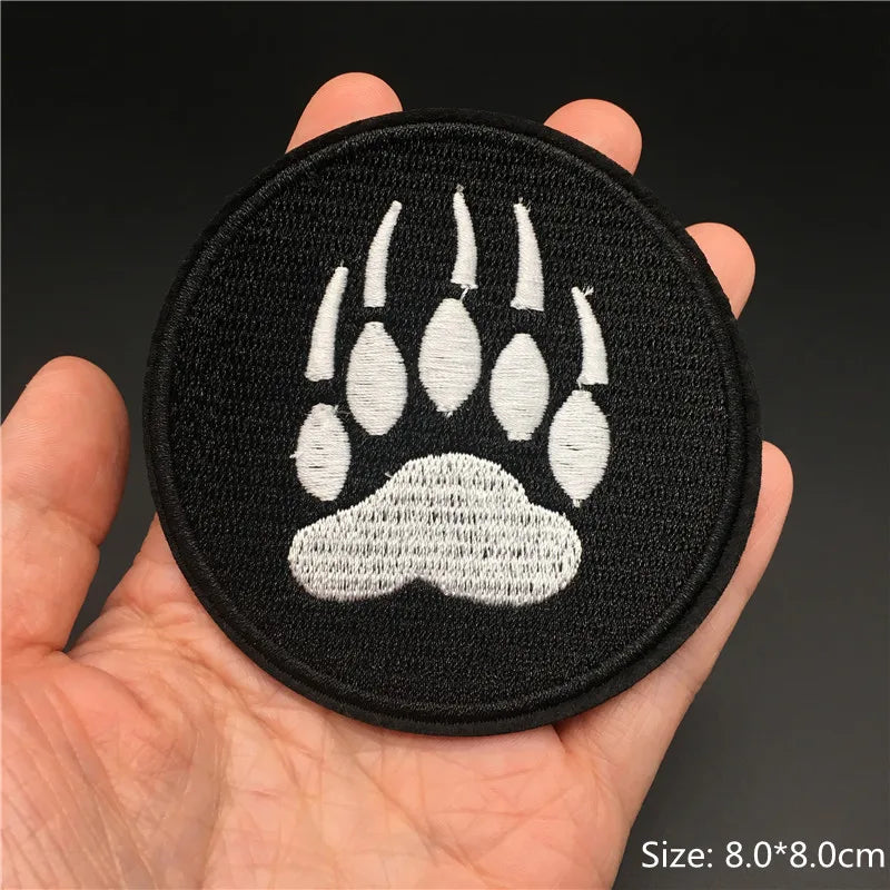 A hand holds a black embroidered paw print patch with white detailing.