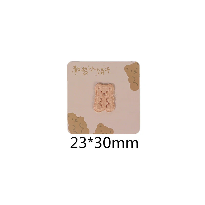 A square beige iron-on patch featuring a light brown embroidered bear design.