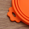 An orange reusable silicone food storage lid with a handle resting on a wooden surface.