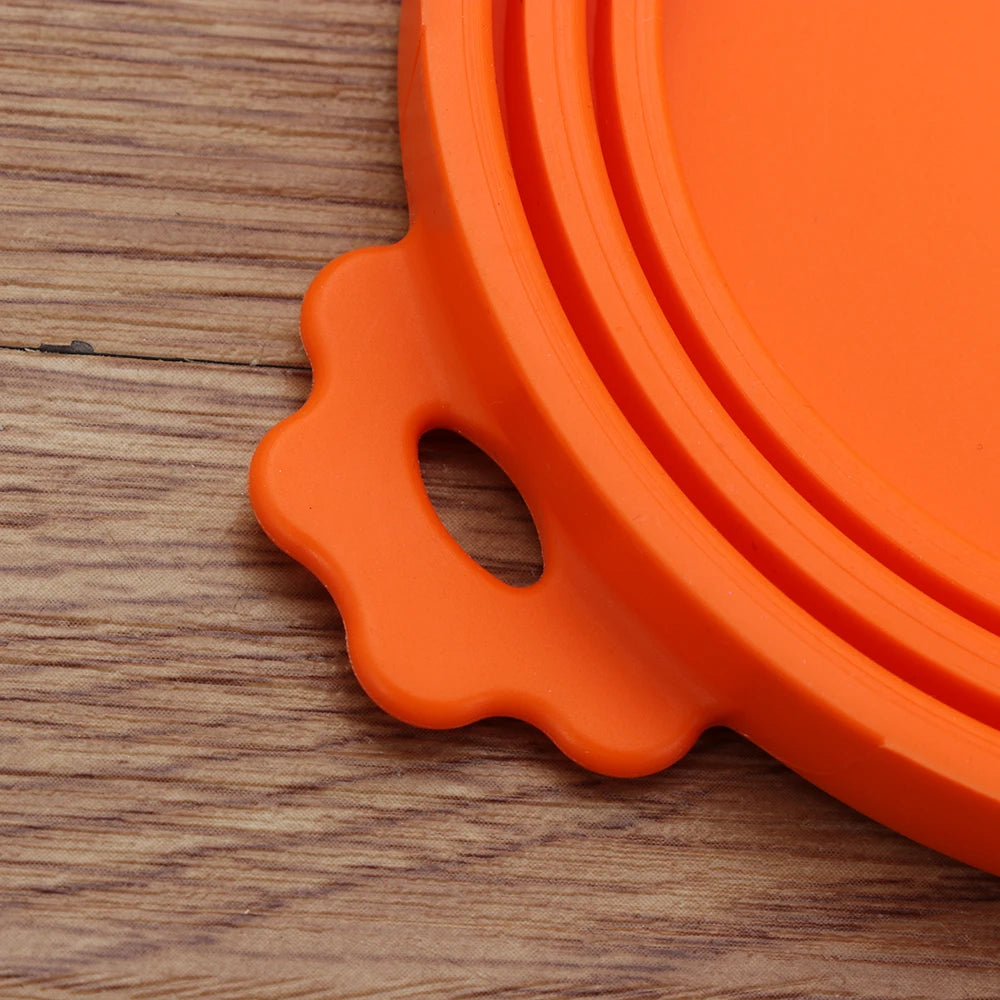 An orange reusable silicone food storage lid with a handle resting on a wooden surface.