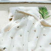 A white coral fleece baby blanket with subtle bear embroidery is displayed on a light beige surface.