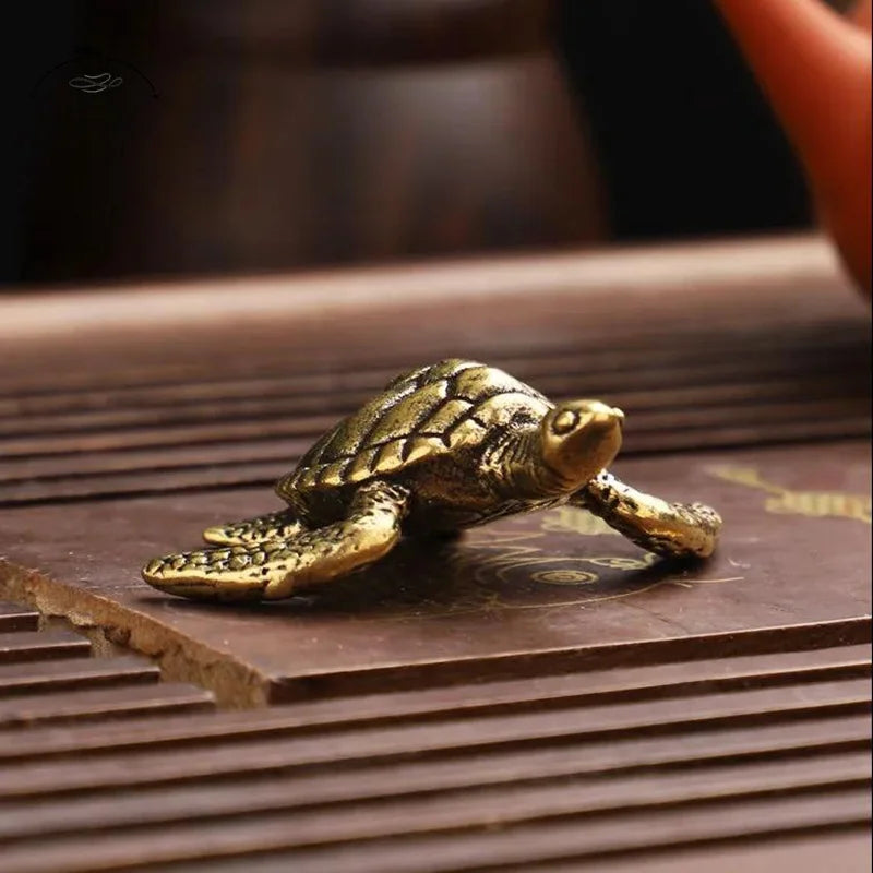 A small, antique-style solid copper turtle figurine resting on a dark wooden surface.
