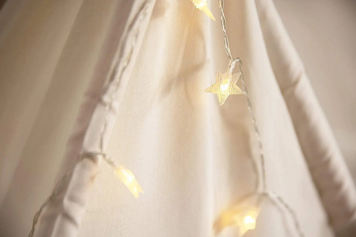 A soft, light-colored fabric tent with string lights and star decorations hanging indoors.