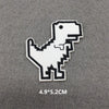 A white embroidered patch shaped like a dinosaur silhouette on a gray fabric background.