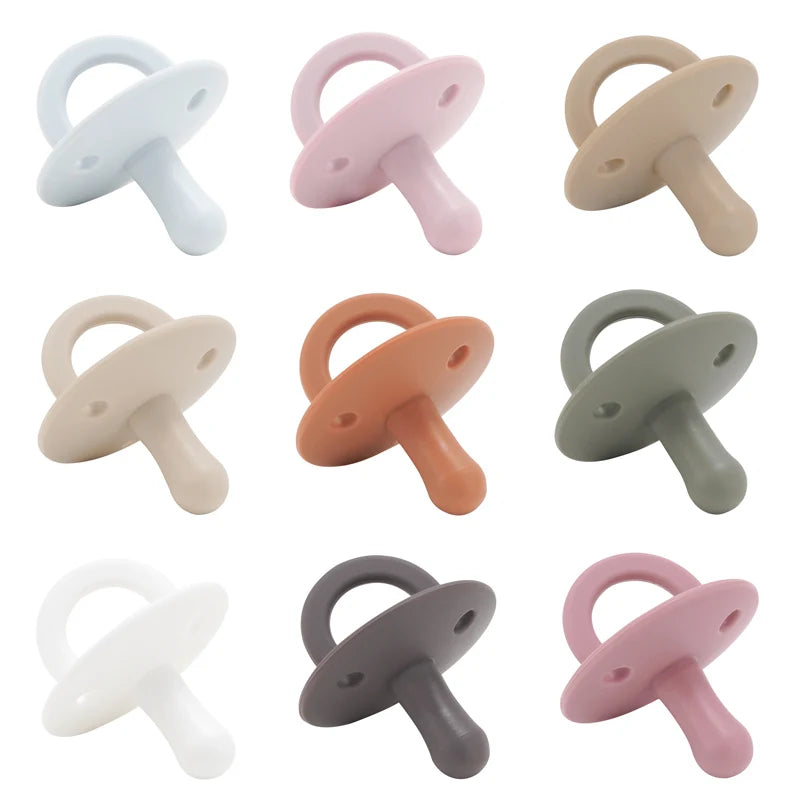 A collection of silicone baby pacifiers or soothers in various pastel colors including white, pink, beige, and gray.