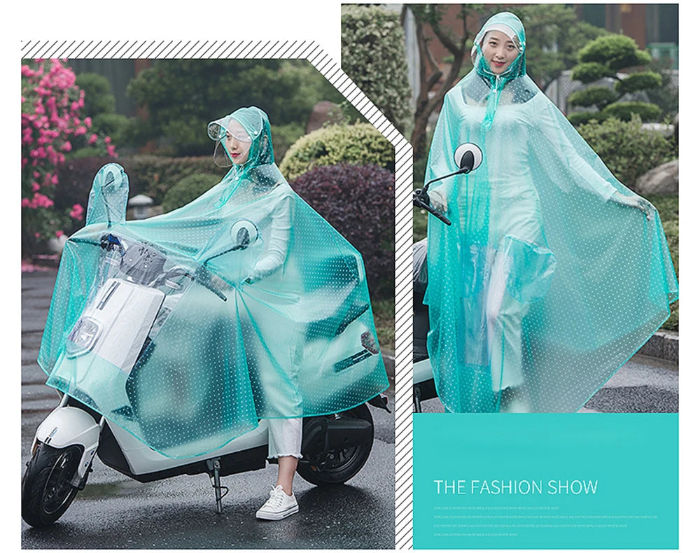 A woman wearing a transparent, iridescent waterproof motorcycle rain poncho with a hood is riding a scooter outdoors.