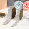 Silver crystal rhinestone ribbon stickers and a gold ribbon are displayed next to fluffy pink and blue pom-pom flowers.