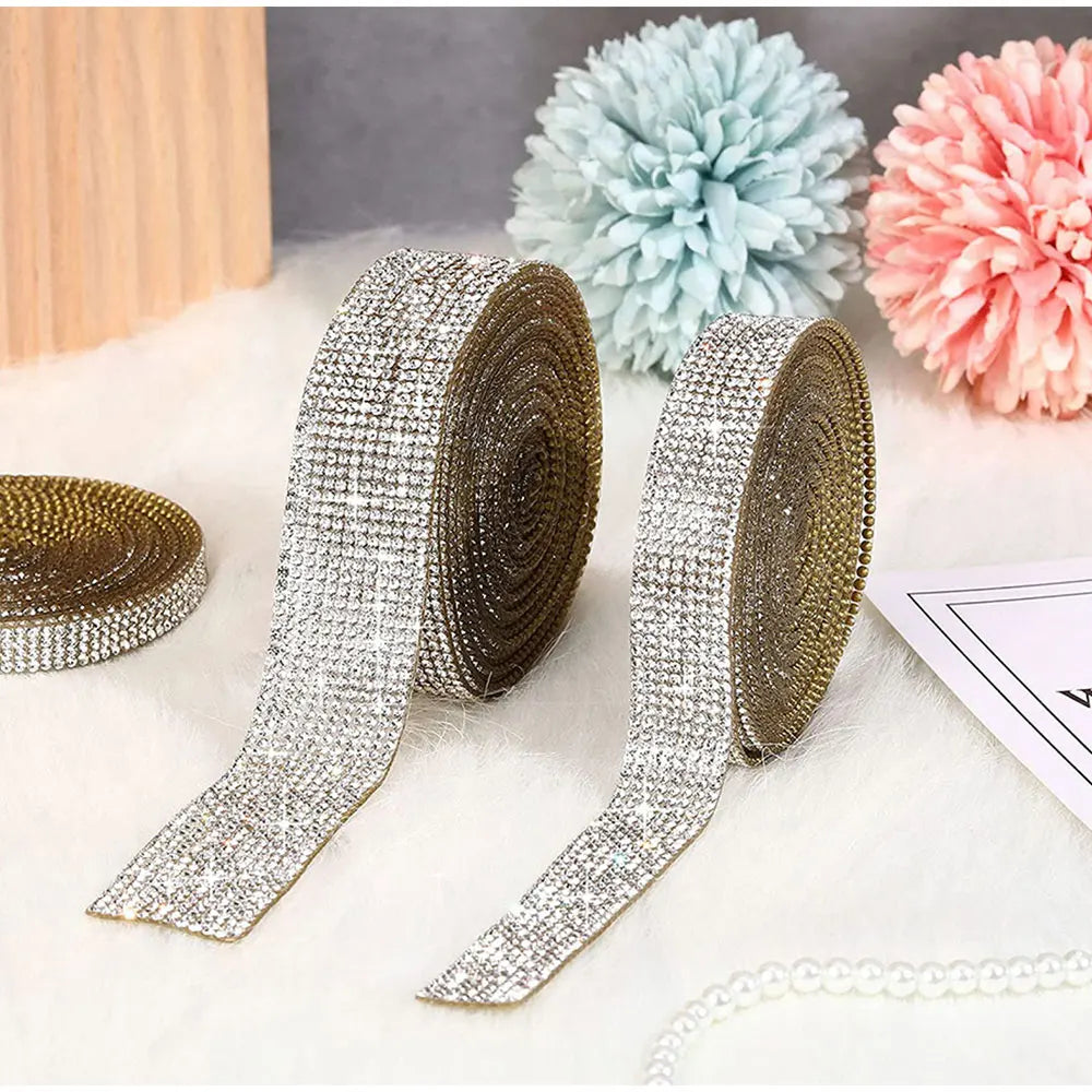 Silver crystal rhinestone ribbon stickers and a gold ribbon are displayed next to fluffy pink and blue pom-pom flowers.