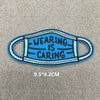 Blue fabric face mask embroidered with the text Wearing is Caring