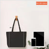 A black foldable canvas tote bag displayed on a white surface next to a tablet and smartphone.