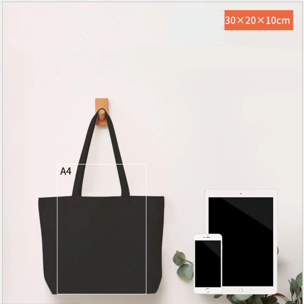 A black foldable canvas tote bag displayed on a white surface next to a tablet and smartphone.