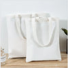 A white canvas tote bag with light beige handles is displayed on a wooden surface.