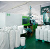White plastic buckets with leakproof lids are stacked on a green shelf in a factory setting.