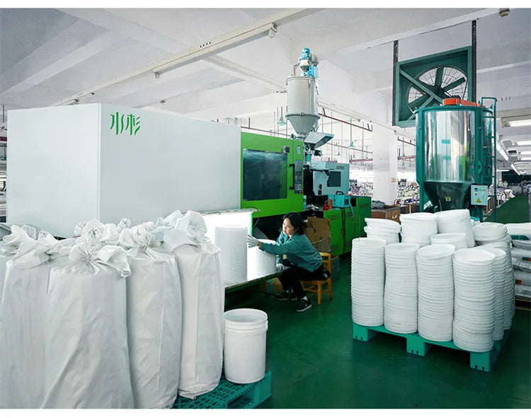 White plastic buckets with leakproof lids are stacked on a green shelf in a factory setting.