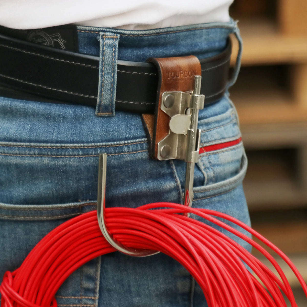 A genuine leather tool holster featuring a steel J-hook attached to a belt, shown against denim jeans.