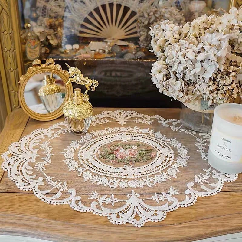 Elegant oval lace embroidered placemat on a wooden table with decorative glass and floral arrangements.