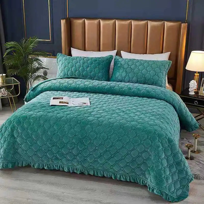 A teal quilted velvet bedspread with a ruffled edge is displayed on a bed in front of a wooden headboard.