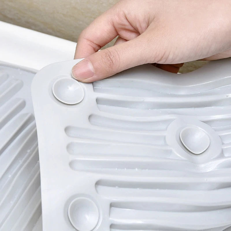 A hand is pressing a silicone washboard with suction cups onto a white plastic surface.